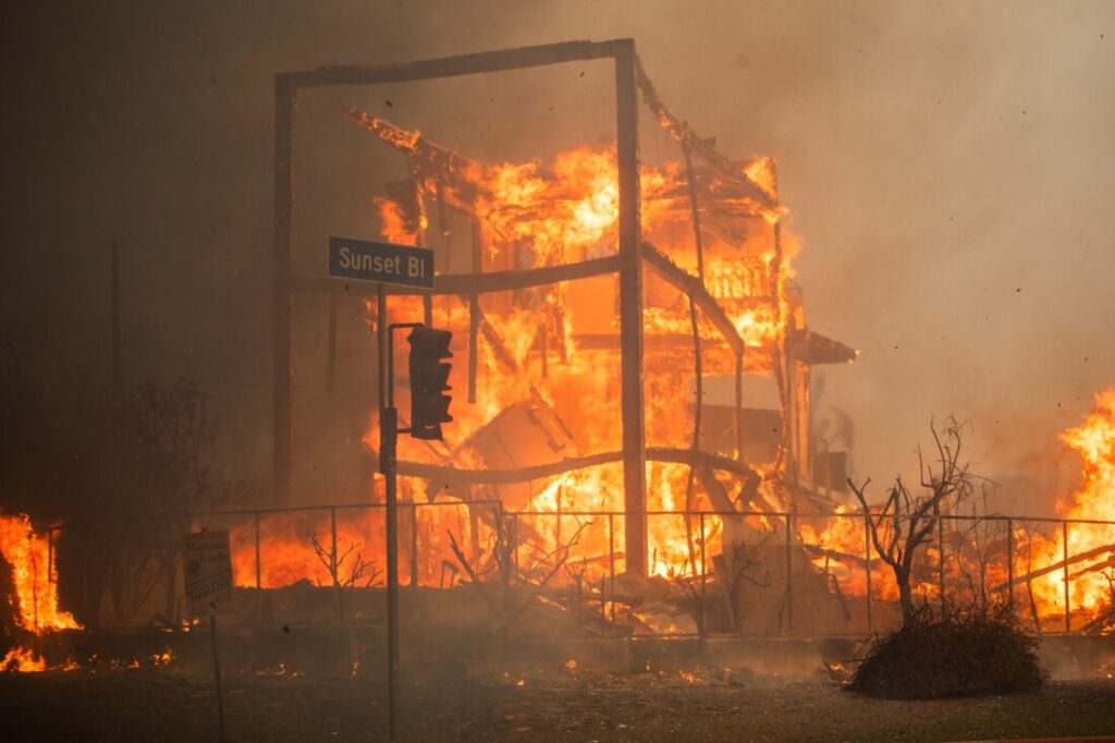 Chamas do Incêndio em Palisades queimam um prédio na Sunset Boulevard durante uma poderosa tempestade de vento na quarta-feira, no bairro de Pacific Palisades, em Los Angeles.